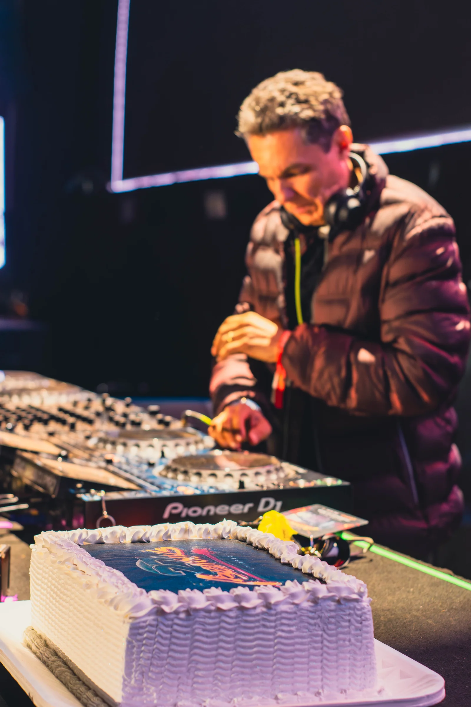 DJ em apresentação diante dos equipamentos e do público, com iluminação de palco.