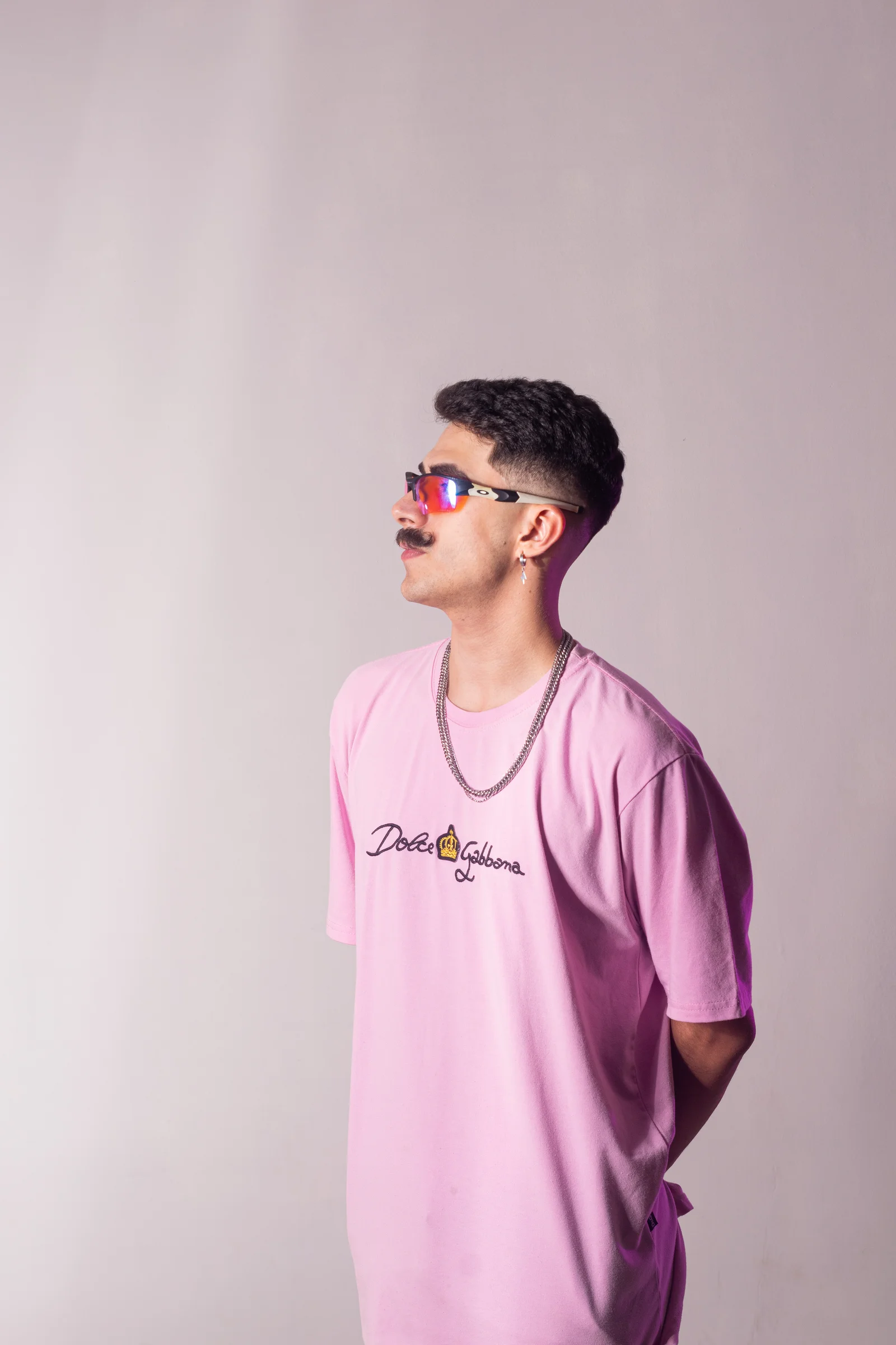 Retrato artístico em estúdio com camiseta lilás, óculos e fundo claro.