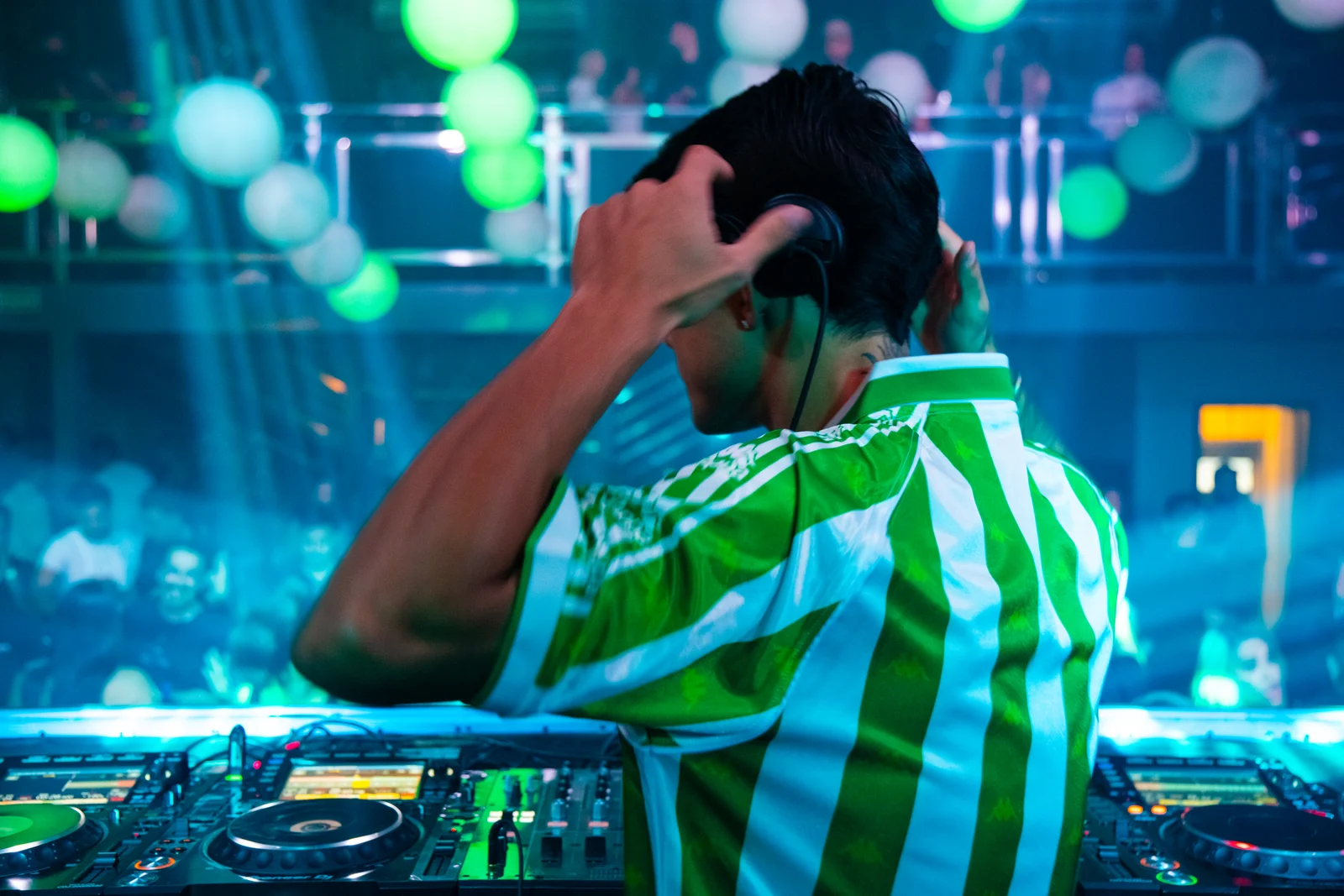 Yuri com fones de ouvido em apresentação, sob iluminação verde e azul.